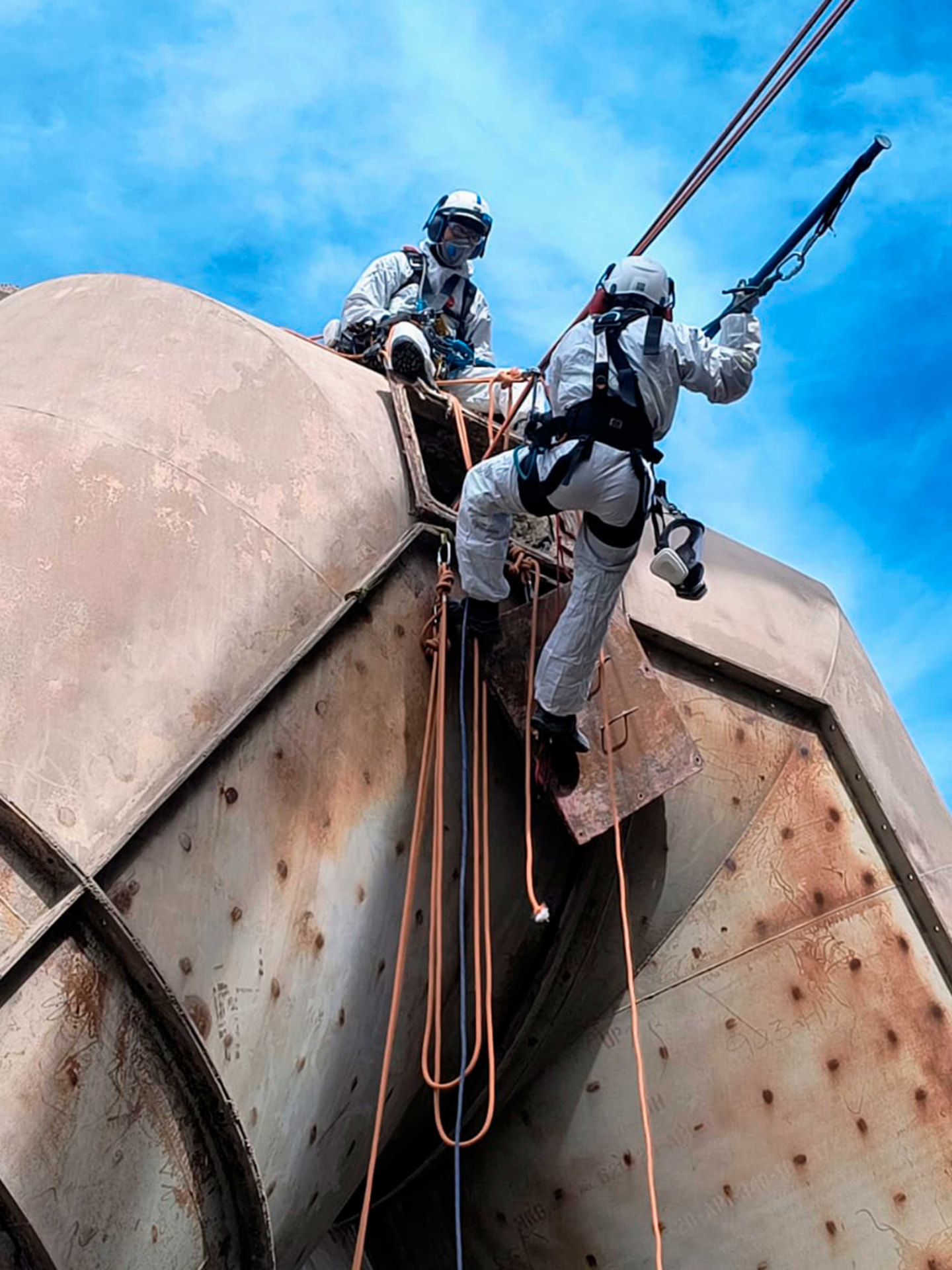 Dois profissionais acessando por cordas o topo de equipamento industrial