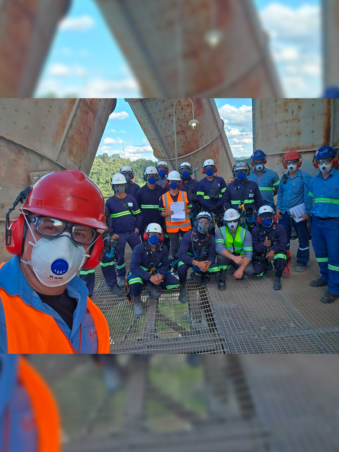 Equipe técnica com EPI reunida sob estrutura metálica de grande porte em planta industrial
