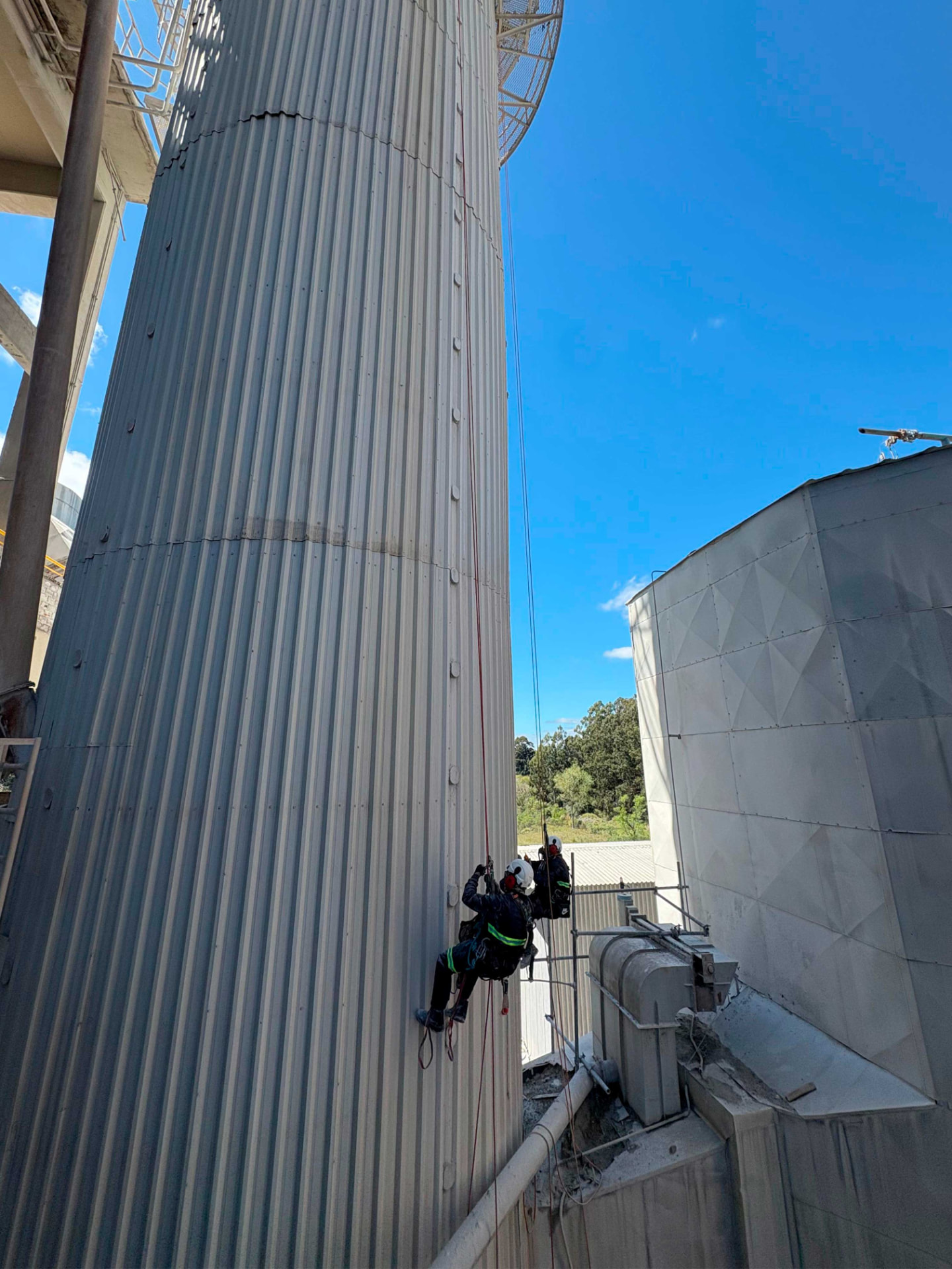 Profissionais em acesso por cordas na lateral de silo industrial de grande altura